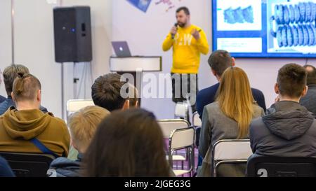 Audience listens to the lecturer at the conference hall. Back view of sitting people and blurred speaker. Stock Photo