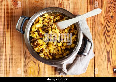 Potatoes fried with garlic and herbs, served in a pan, wooden background Stock Photo