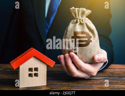 Man holds out a philippine peso bag near the house. Bank approval for issuing a mortgage loan. Property appraisal. Favorable terms and conditions, low Stock Photo