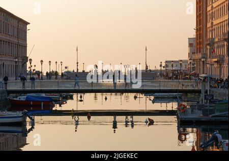 TRIESTE, Italy - March 25, 2022: Life on the Canal Grande at sunset, with a pedestrian bridge in the foreground Stock Photo