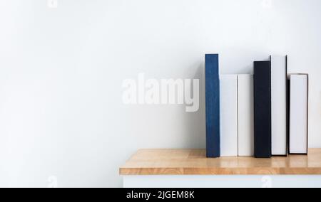 Mockup of white and blue blank book spines on wooden shelf on white background with copy space. Row of books with empty space book names cover, minima Stock Photo