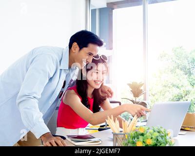 Asian couple, young woman and man looking and pointing at laptop computer screen on desk together for travel booking, flight, hotel room and trip info Stock Photo