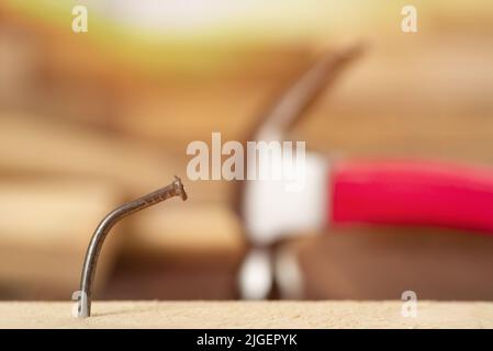 A bent nail in a wooden board with a hammer in the background. Stock Photo