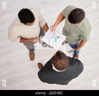 The answers lie in the numbers. High angle shot of three unrecognizable businessmen looking over paperwork while standing in the office. Stock Photo