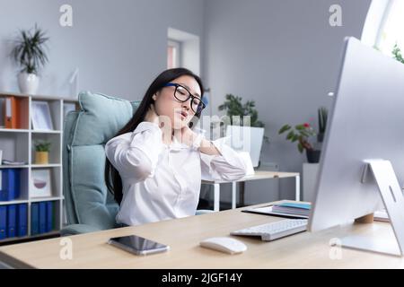 Young beautiful Asian woman office worker, freelancer, business woman in glasses and white shirt, sitting at the table at the computer, tired, exhaust Stock Photo