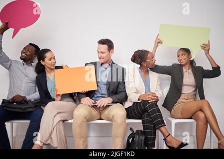 Weve got something to say. a group of young businesspeople holding speech bubbles while waiting in line. Stock Photo