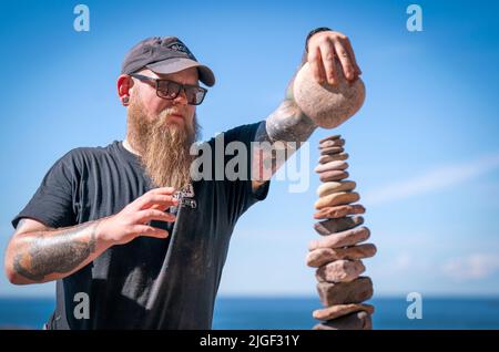 Competitor Aaron Tierney from Falkirk takes part in the 'most stones balanced in 20 minutes' event during the European Stone Stacking Championships 2022 on Eye Cave Beach in Dunbar, East Lothian. The championships are Europe's largest competition for all stone stacking and rock balancing enthusiasts and artists. Picture date: Sunday July 10, 2022. Stock Photo