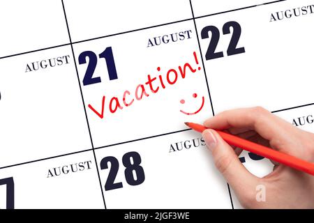 21st day of August. A hand writing a VACATION text and drawing a smiling face on a calendar date 21 August. Vacation planning concept. Summer month, d Stock Photo