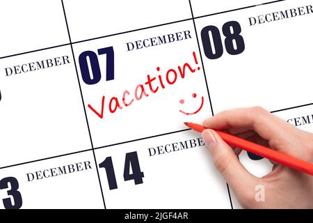 7th day of December. A hand writing a VACATION text and drawing a smiling face on a calendar date 7 December. Vacation planning concept. Winter month, Stock Photo