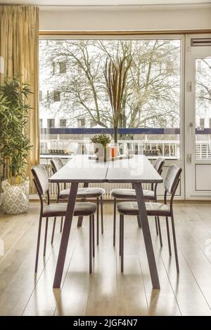 Wooden table with vase and chairs placed near window in light dining room at home Stock Photo