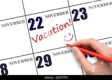 22nd day of November. A hand writing a VACATION text and drawing a smiling face on a calendar date 22 November. Vacation planning concept. Autumn mont Stock Photo