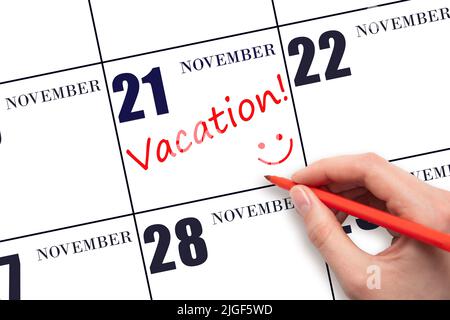 21st day of November. A hand writing a VACATION text and drawing a smiling face on a calendar date 21 November. Vacation planning concept. Autumn mont Stock Photo