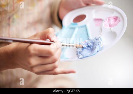 Mixing her own colours. High angle shot of a paint palette in an unrecognizable womans hand while she paints. Stock Photo