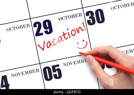 29th day of October. A hand writing a VACATION text and drawing a smiling face on a calendar date 29 October. Vacation planning concept. Autumn month, Stock Photo