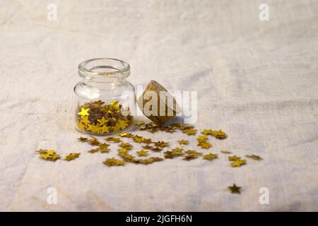 Sequins tube scattered gold stars glitter on rough linen textured background close up top view Stock Photo