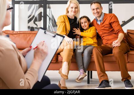 Rear view of female psychologist helping young family with a kid to solve child development problems. Family sitting on a sofa Stock Photo