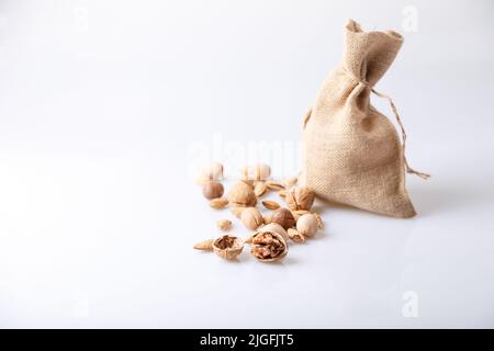 Assorted nuts in the shell on a white background: walnuts, pecans, almonds, macadamia. Nuts in a burlap bag. Selective focus, close-up. Place for text Stock Photo