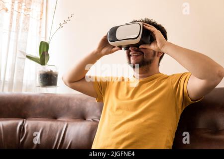 A Latin mid-adult man is wearing a VR Headset and he is sitting on the sofa Stock Photo