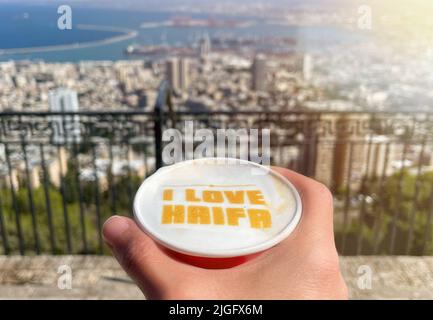 The caption I LOVE HAIFA in a cup of coffee and a view of Haifa city in the background. Stock Photo