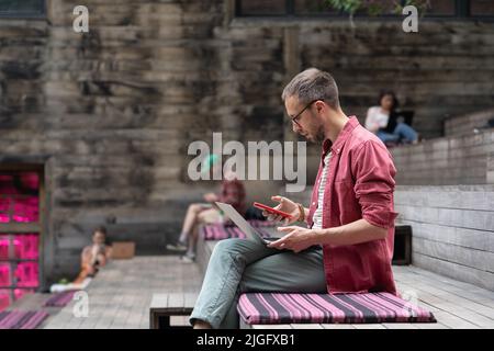 Focused ui ux designer looking at smartphone screen, distracted by his gadget during working Stock Photo