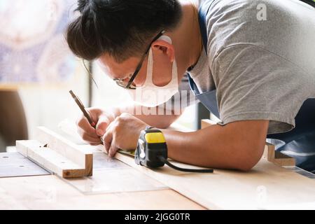 A carpenter measures the planks to assemble the parts and build a wooden table for the customer Stock Photo