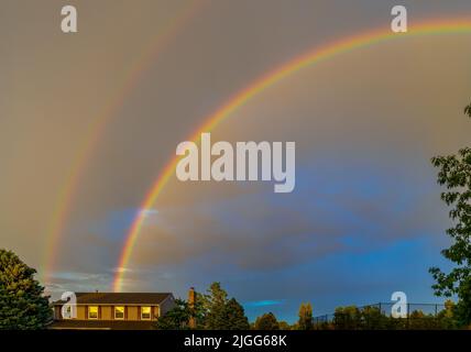 Double rainbow after the rain over the roof of rural house and trees in Aurora, Colorado Stock Photo