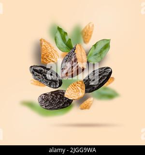 Tonka beans and green leaves float on a beige background. Flying Dipteryx odorata is known as tonka beans for pastry, confectionery business, baking Stock Photo
