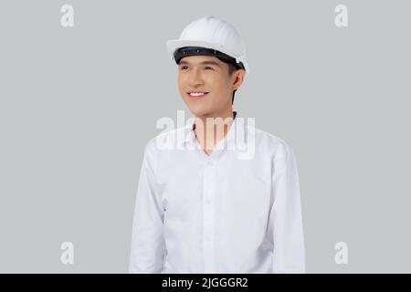 Portrait young asian man is engineer wearing helmet standing and holding blueprint with confident isolated on white background, handsome male is archi Stock Photo