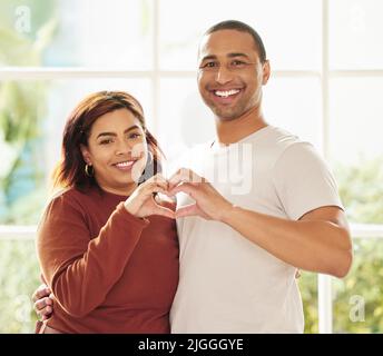 Love lives in this home. a young couple standing inside together and making a heart-shaped gesture. Stock Photo