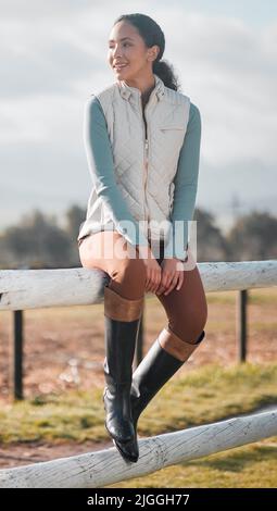 This is the life. Full length shot of an attractive young woman sitting alone on a wooden fence on a farm. Stock Photo