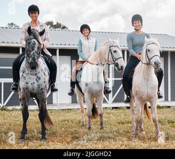 On horseback. Full length portrait of three attractive young women horse riding on a farm. Stock Photo