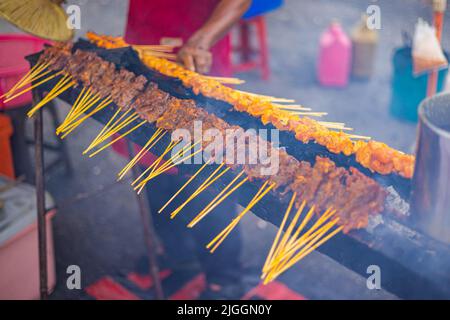 A grill rack on an open fire With satay or sate sticks. Traditional Satey is a meat skewer. Sate is a grilled dish originally from Indonesia but very Stock Photo