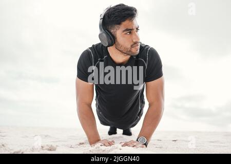 Your workouts can be fun, just add music. a sporty young man wearing headphones while doing push ups on the beach. Stock Photo