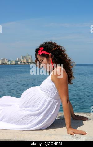 Profile view of eight-month pregnant woman with ocean and city behind Stock Photo