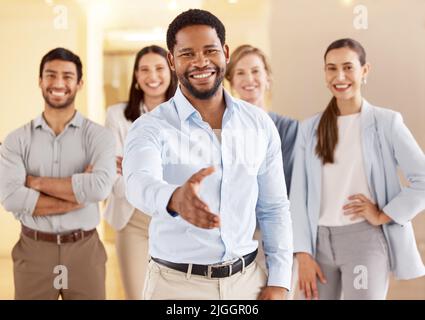 Dont stand around and wait for opportunity - create it. Portrait of a young businessman extending a handshake in an office with his colleagues in the Stock Photo