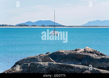 A luxury catamaran at anchor off shore from oyster covered rocks at Bowen, Queensland, Australia. Stock Photo