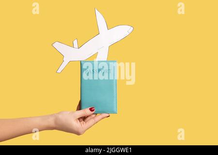 Closeup of woman hand holding paper plane and passport, advertise of airline service, plane landing or departure, vacation abroad. Indoor studio shot isolated on yellow background. Stock Photo