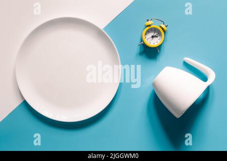 Empty plate, cup and alarm clock on a blue background. Stock Photo