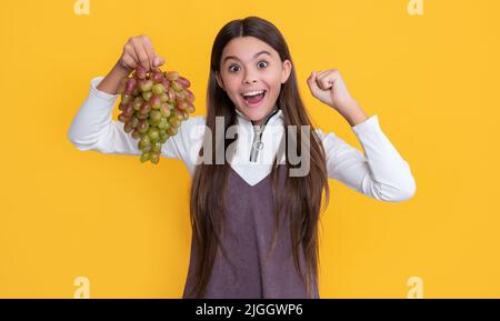 surprised amazed child holding fresh grapes fruit on yellow background Stock Photo