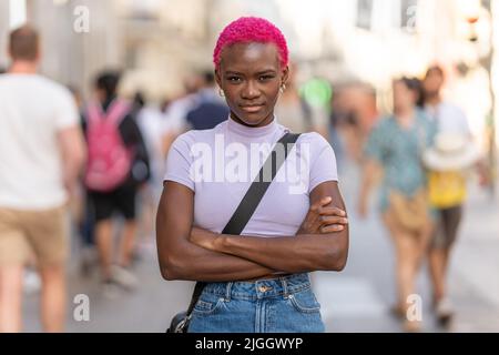 Serious afro woman looking at camera with arms crossed outdoors Stock Photo