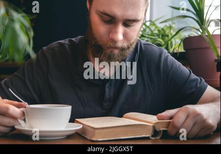 A young man reads a book over a cup of tea in a cafe. Stock Photo