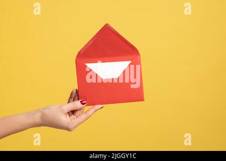 Profile side view closeup of woman hand holding red opened letter envelope, romantic message. Indoor studio shot isolated on yellow background. Stock Photo