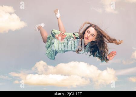 Beautiful girl levitating in mid-air, falling down and her hair messed up soaring from wind, model flying hovering with dreamy peaceful expression in sky. collage composition on day cloudy blue sky Stock Photo