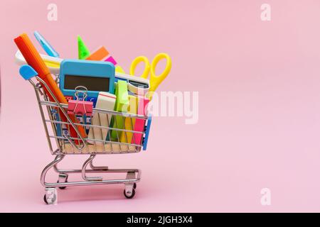Blue shopping cart or trolley and stationery pen pencil clip pin rubber isolated on pink background. Online shopping concept for school Stock Photo