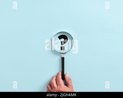Male hand holds a magnifying glass or magnifier focusing on a question mark. Focusing on a problem, solution, research, searching or discovery concept Stock Photo