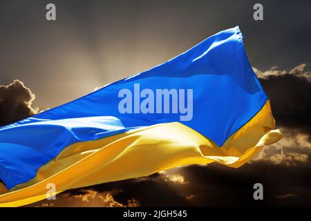 Sunlight flag of Ukraine waving on sunset peaceful sky with danger clouds. Stop war! Stock Photo