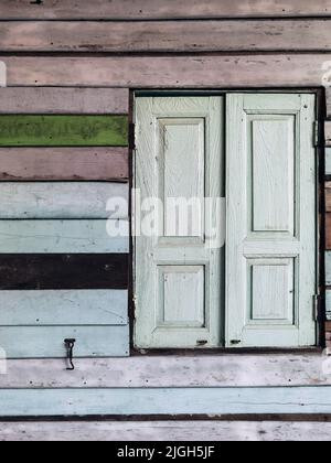 Old grunged wooden window frame painted white vintage with old colourful plywood wall. Antique window frame and old panes. Old closed window and plank Stock Photo