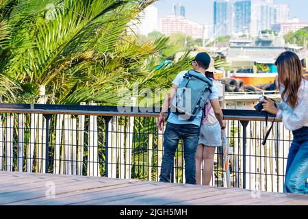 Back view of Asian couple relaxing and chilling at a riverside. Relaxed lifestyle for lover enjoying freedom in summer holidays. Happy people outdoors Stock Photo