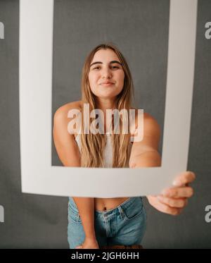 Caucasian female arm stretched out holding a white frame smiling Stock Photo