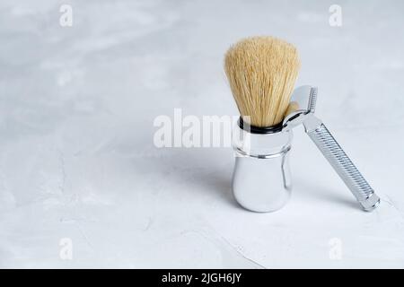 Traditional chrome-plated safety razor and a shaving brush isolated on a concrete table with copy space. Stock Photo